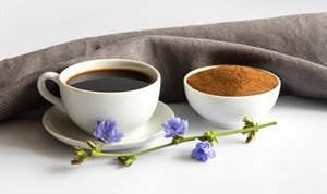 Cup of chicory coffee beside a bowl of ground chicory and blue chicory flowers
